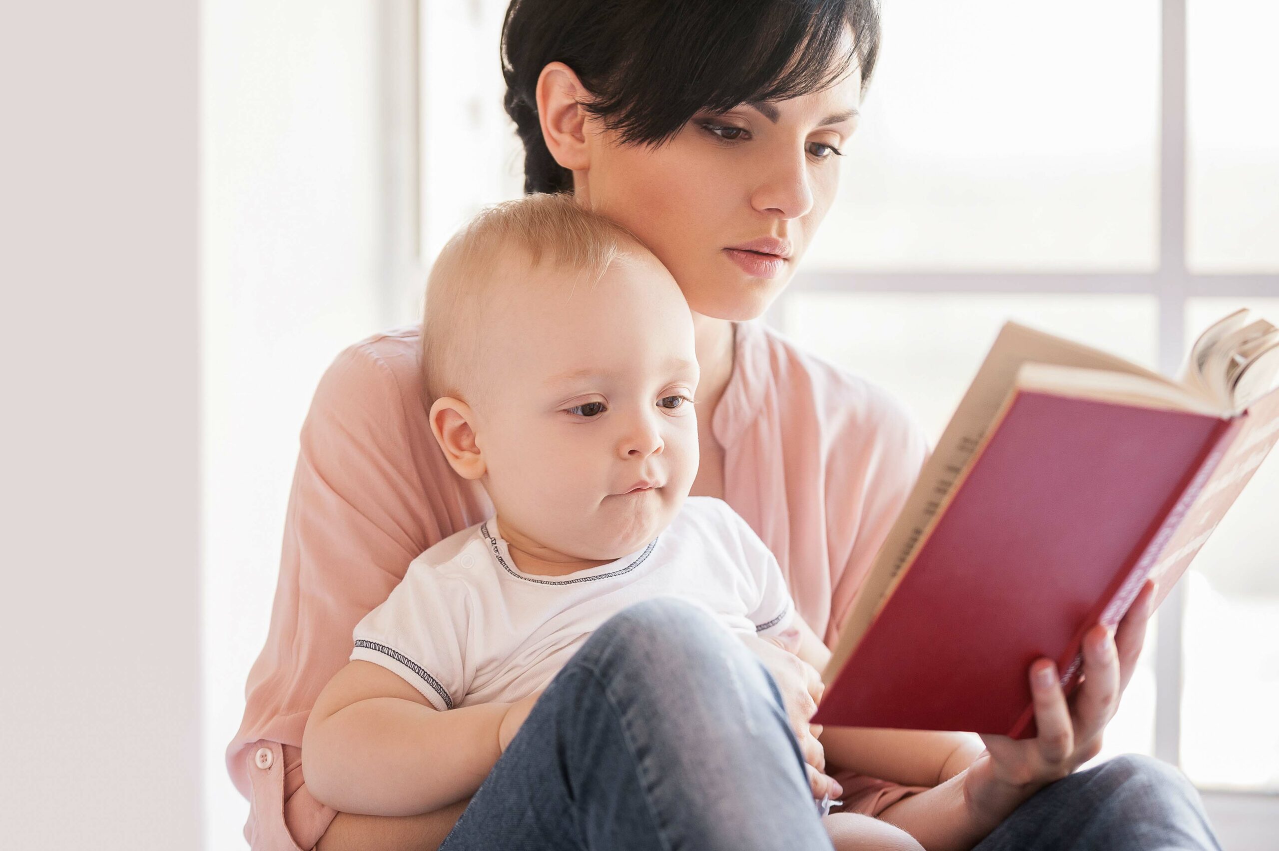 Mother reading a book with a baby in her lap.